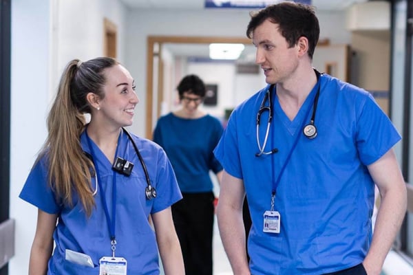 2 Trainee doctors in scrubs walking in corridor